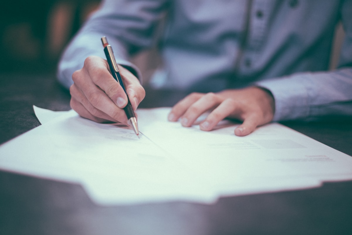 Person signing documents at a desk with paperwork